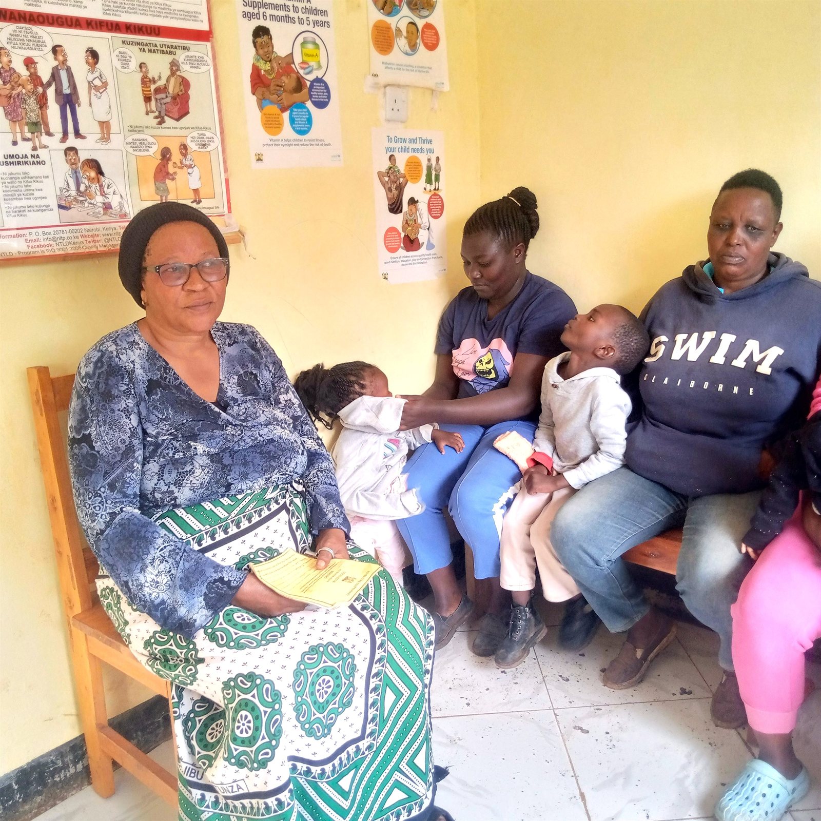 A nurse weighing babies with their mothers at a local health facility